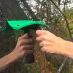 raclette portée par une main à son manche qui est sur un carrosserie de voiture noir